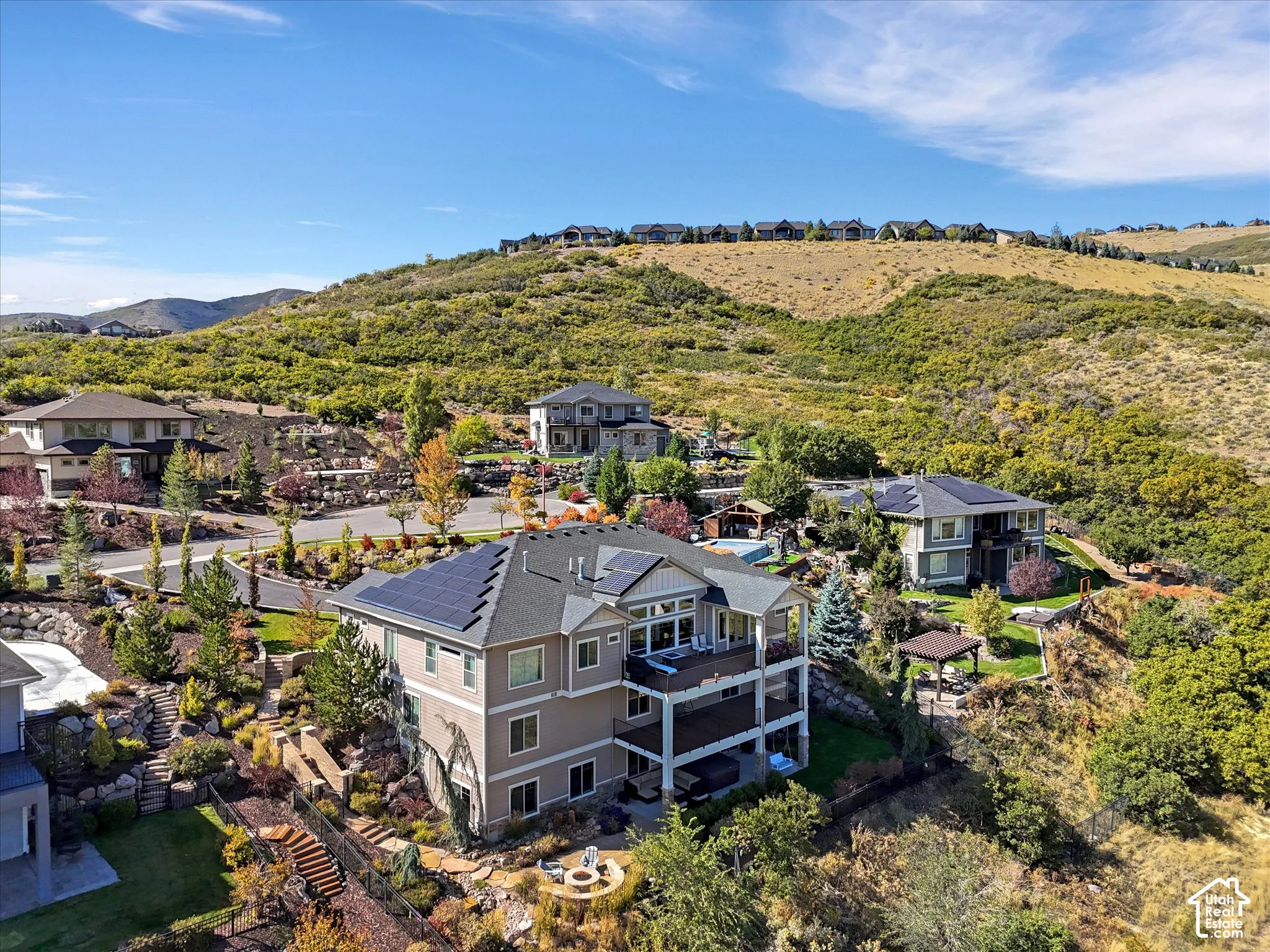 Multi-level residence featuring solar panels, tiered stone landscaping, dual-level covered decks, and a circular stone fire pit