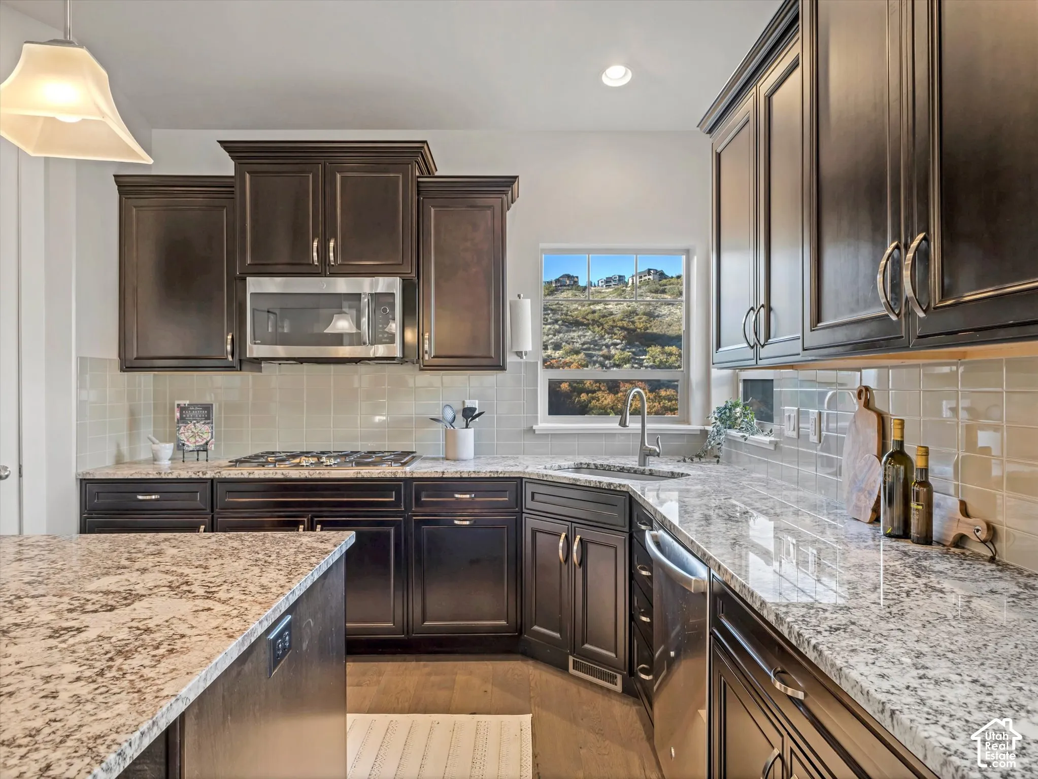 Kitchen featuring dark-finish cabinetry, stone-surface countertops, light-toned tiled backsplash, stainless steel appliances, and wood-finish flooring