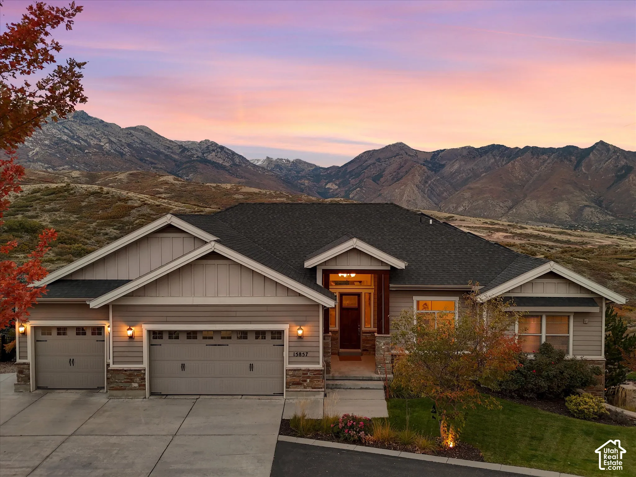 Single-story residence featuring horizontal lap siding, stone veneer accents, a multi-gabled roofline, an attached three-car garage, and a backdrop of mountain scenery