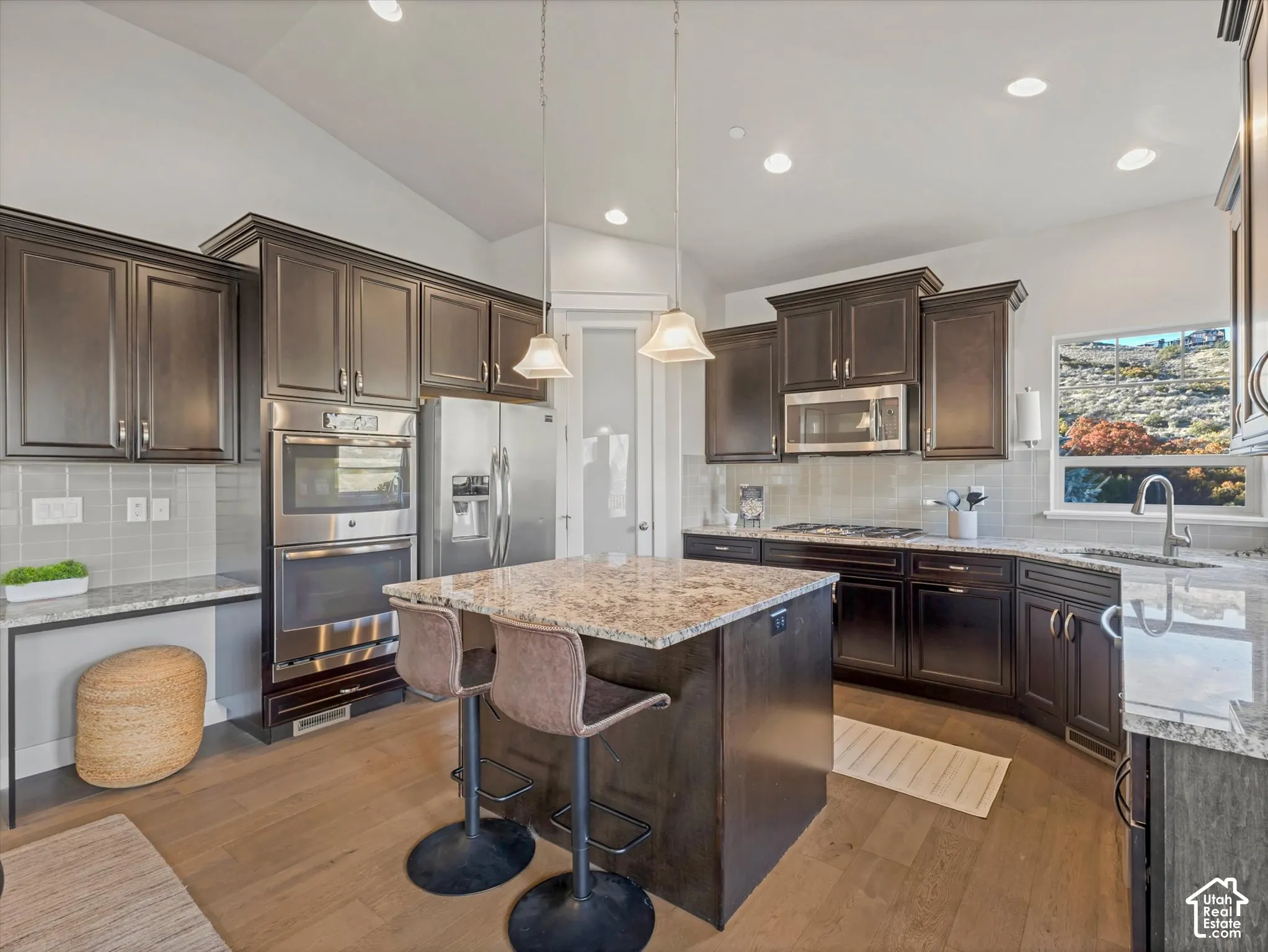 Kitchen featuring dark wood cabinetry, stone countertops, stainless steel double wall ovens, a central island, and wood-finish flooring