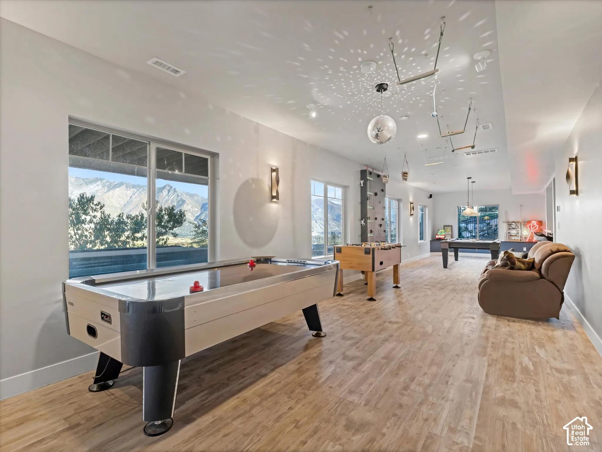Spacious interior featuring wood-finish flooring, recessed lighting, wall-mounted sconces, large windows with mountain scenery, and a built-in climbing wall