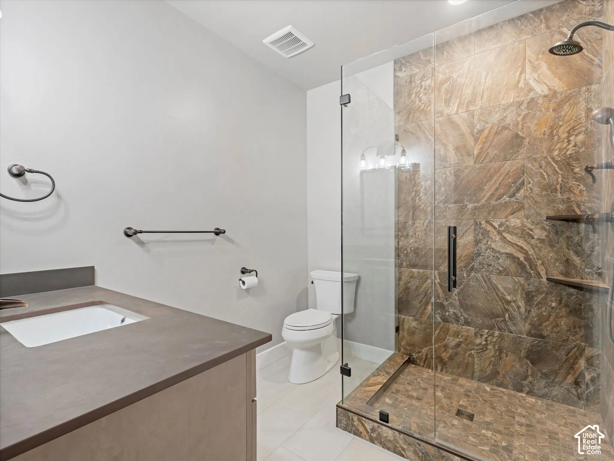 Bathroom featuring a walk-in shower with floor-to-ceiling tile surround, glass enclosure, built-in shelving, and a dark-toned vanity countertop