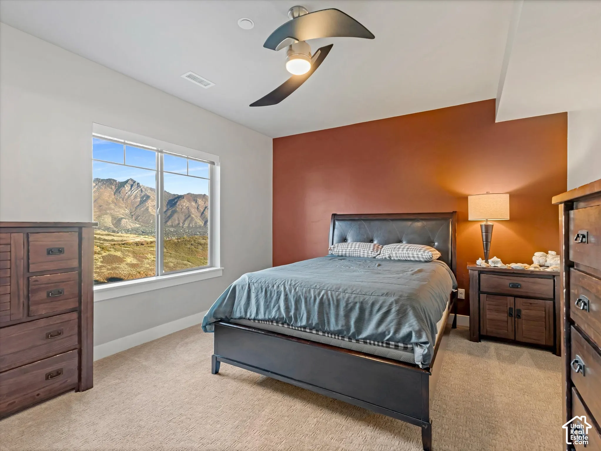 Room featuring neutral carpeting, an accent wall, a multi-blade ceiling fan, and a large window showcasing a mountain landscape