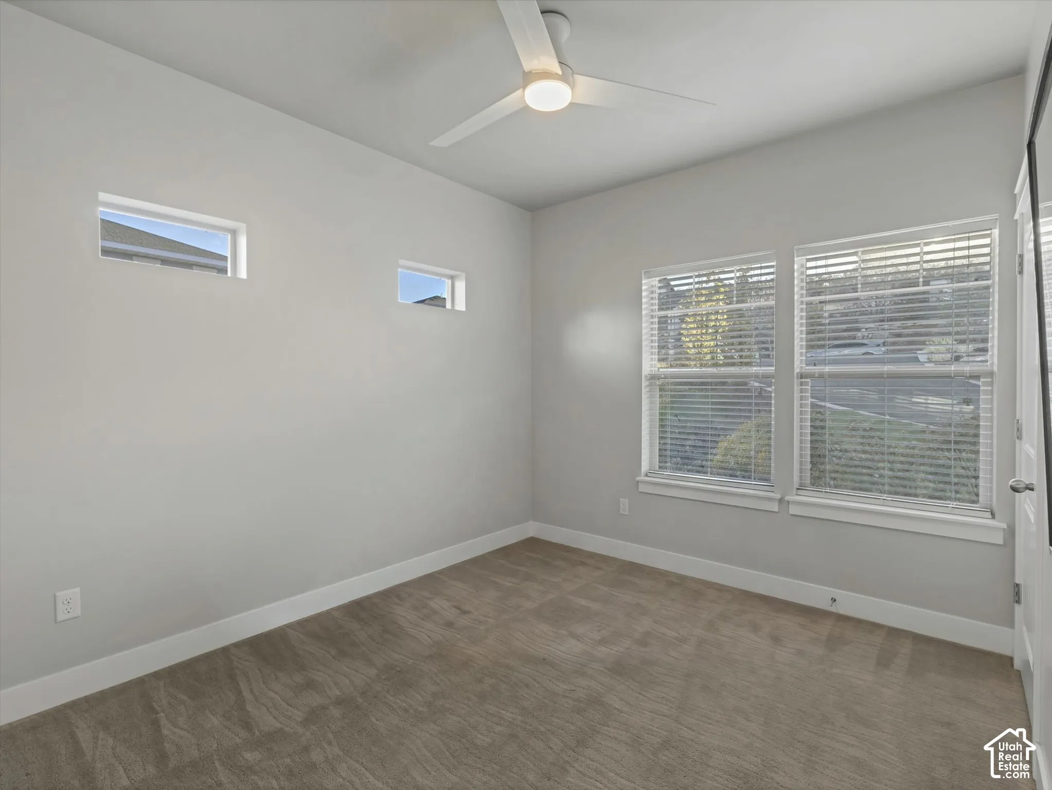 Neutral wall tones, carpeting, high-placed clerestory windows, dual-panel windows with blinds, and a white ceiling fan with integrated lighting