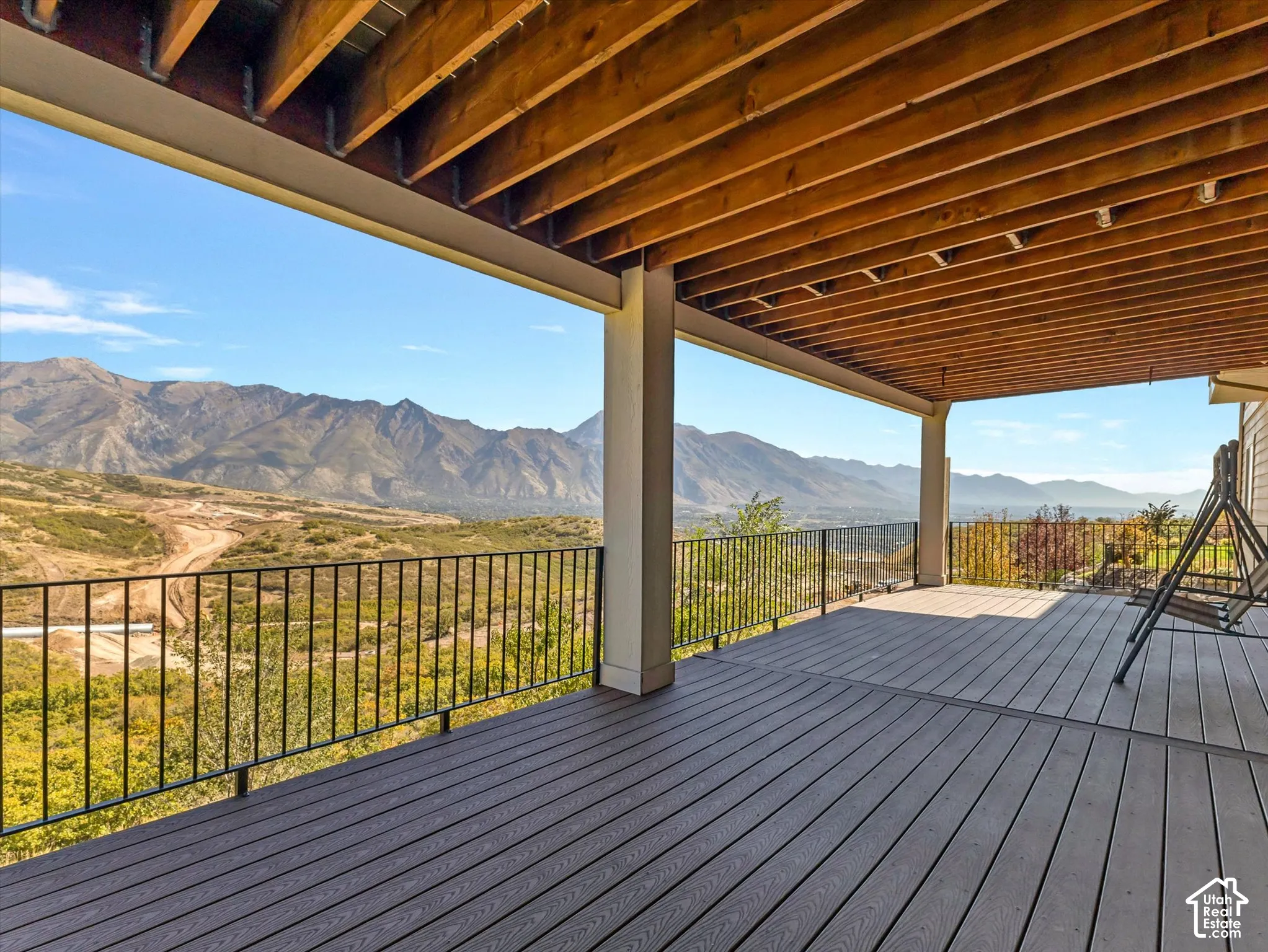 Covered deck featuring wood-beam ceiling, composite decking, black metal railing, and mountain backdrop