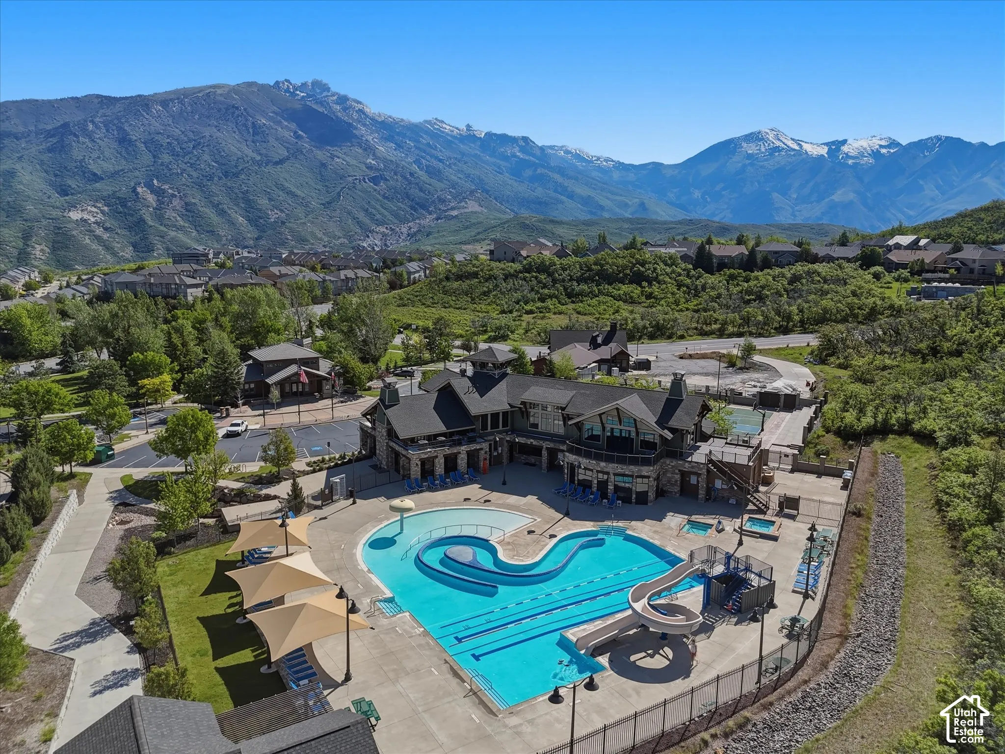 Recreational facility featuring a swimming pool with lap lanes and a slide, dedicated hot tub, expansive concrete decking, shade structures, and mountain backdrop