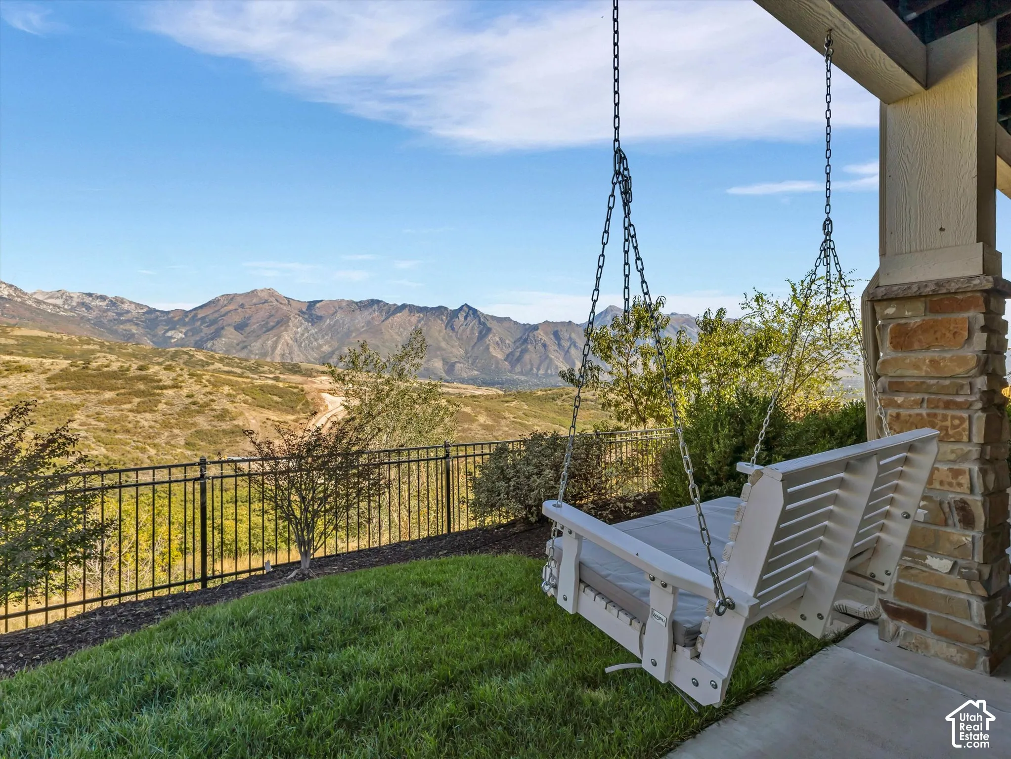 Covered patio featuring stone-clad pillars, concrete flooring, and a metal perimeter fence against a mountain backdrop