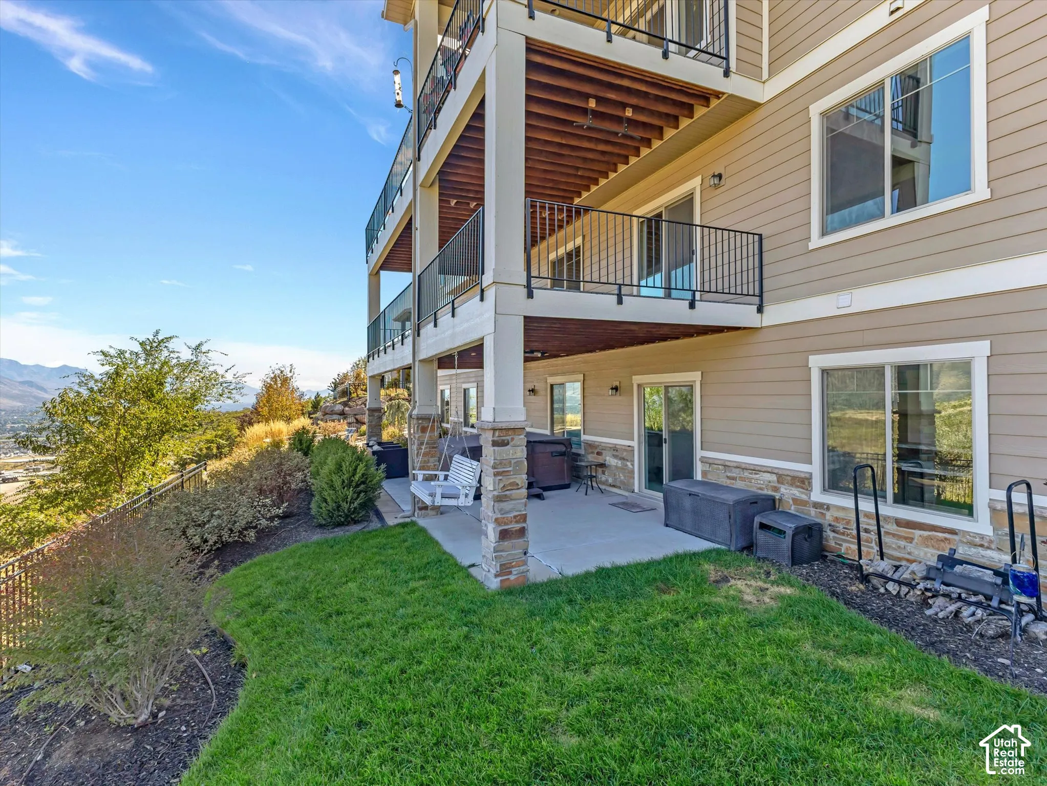 Multi-level deck with metal railings, covered concrete patio, stone veneer siding, and tiered landscaping