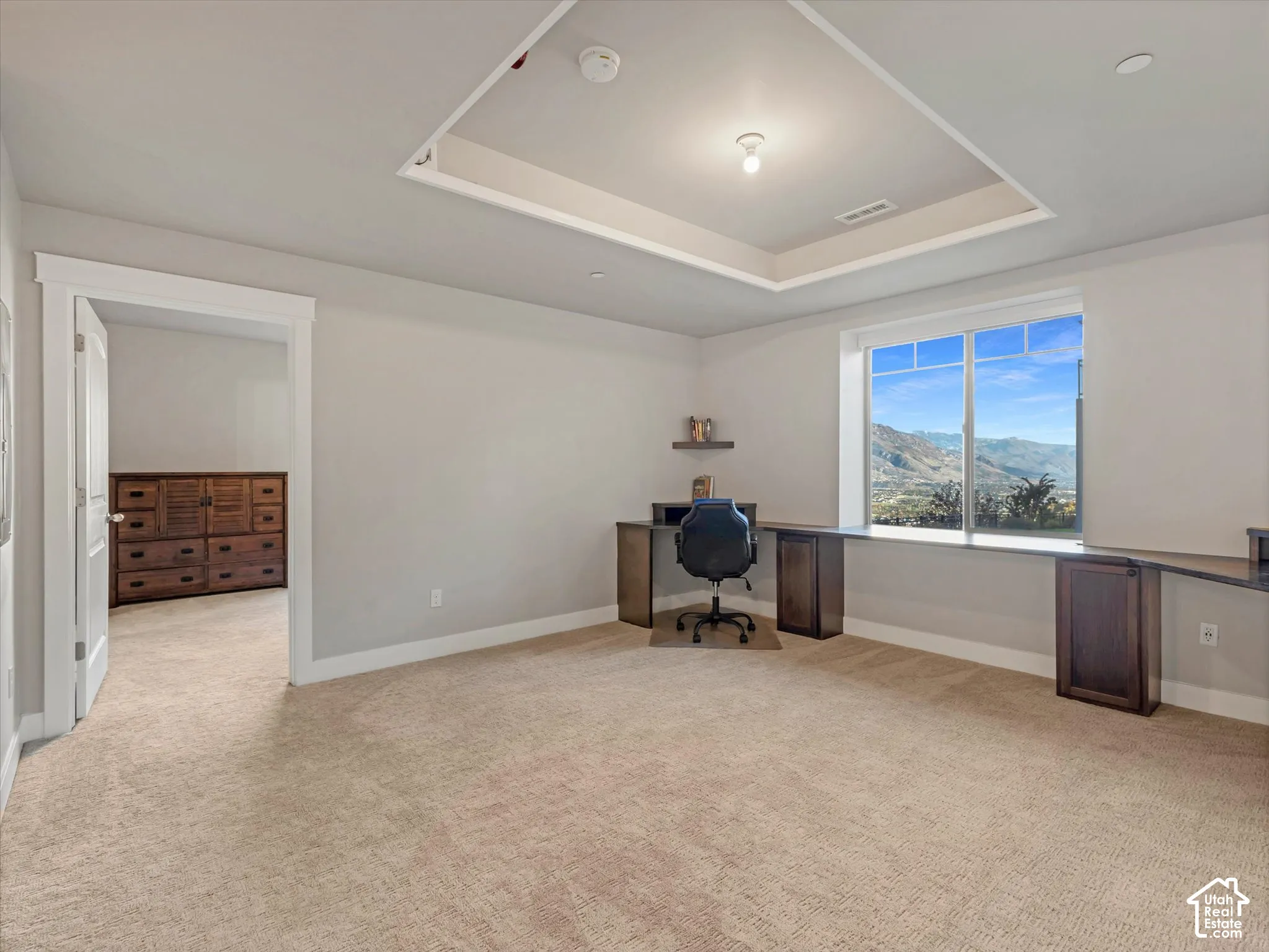Room featuring a tray ceiling, wall-to-wall carpeting, built-in cabinetry with a desk surface, and window-framed mountain scenery