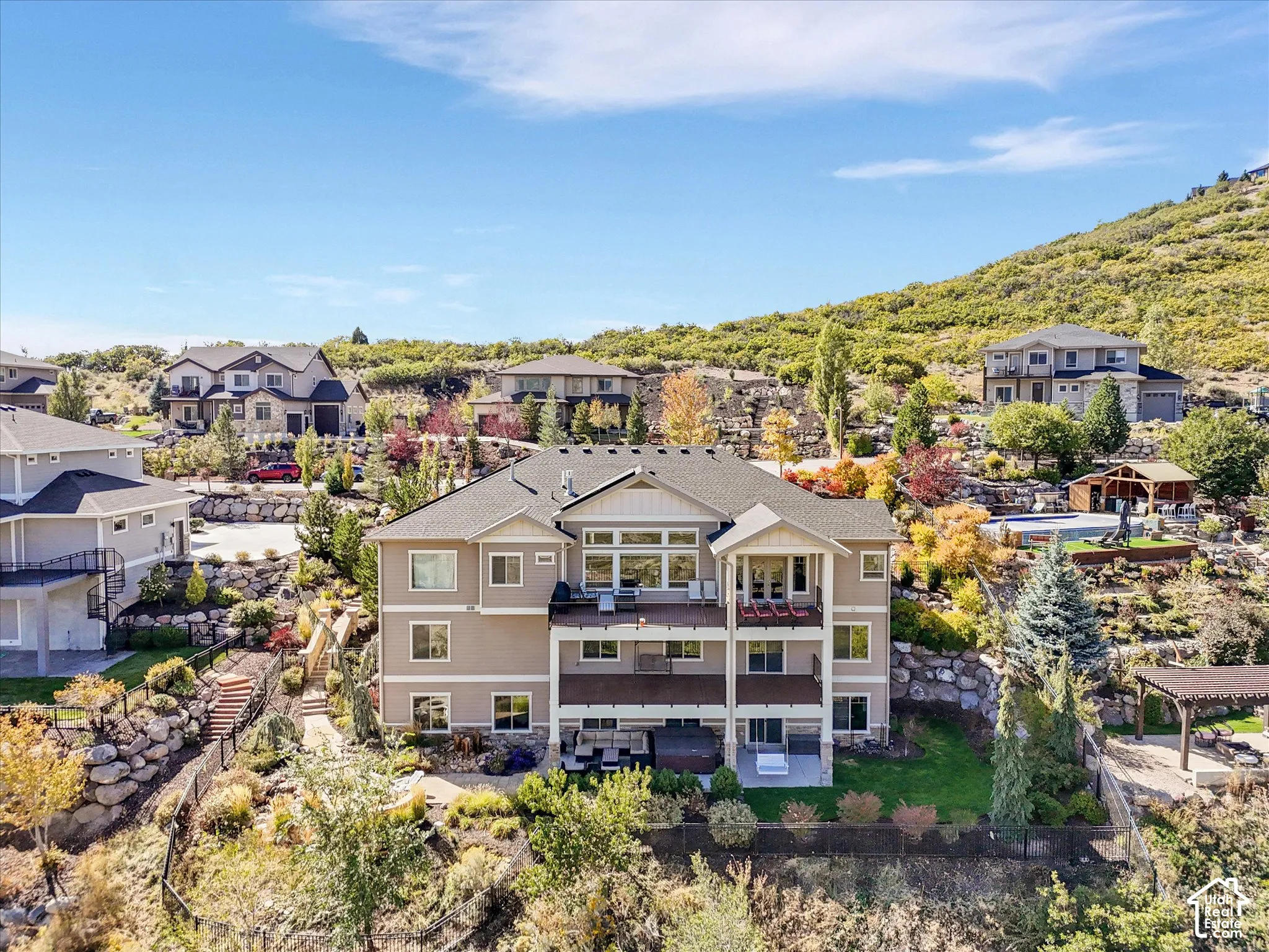 Multi-level residential exterior featuring two stacked rear decks, integrated stone landscape retaining walls, a manicured lawn, and expansive mountain terrain