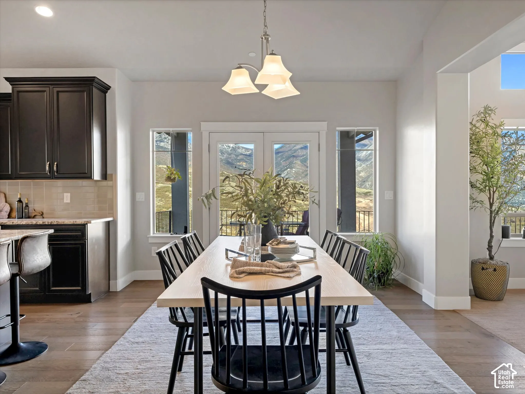Dining area featuring dark cabinetry, neutral backsplash, wood-finish flooring, a multi-light chandelier, and double glass doors revealing mountain scenery