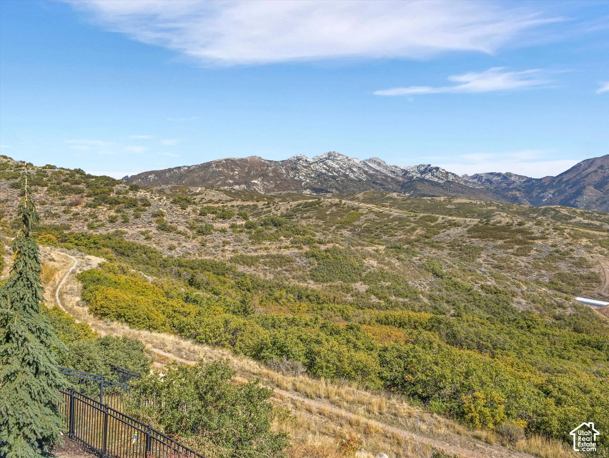 Expansive landscape featuring rugged mountain terrain, rolling hills, native scrub oak vegetation, and metal perimeter fencing