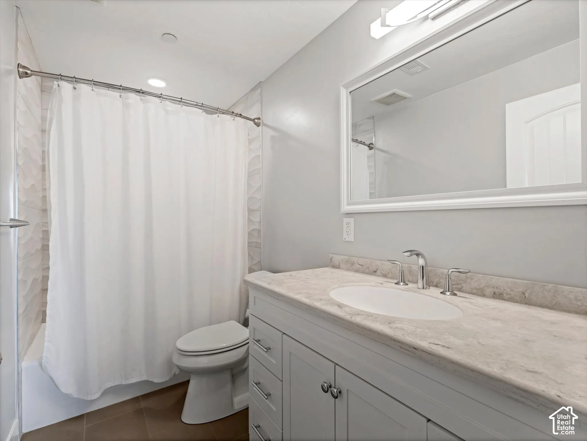 Bathroom featuring a grey shaker-style vanity with stone-finish countertop, undermount sink, framed wall mirror, and tiled shower surround with decorative textured accents