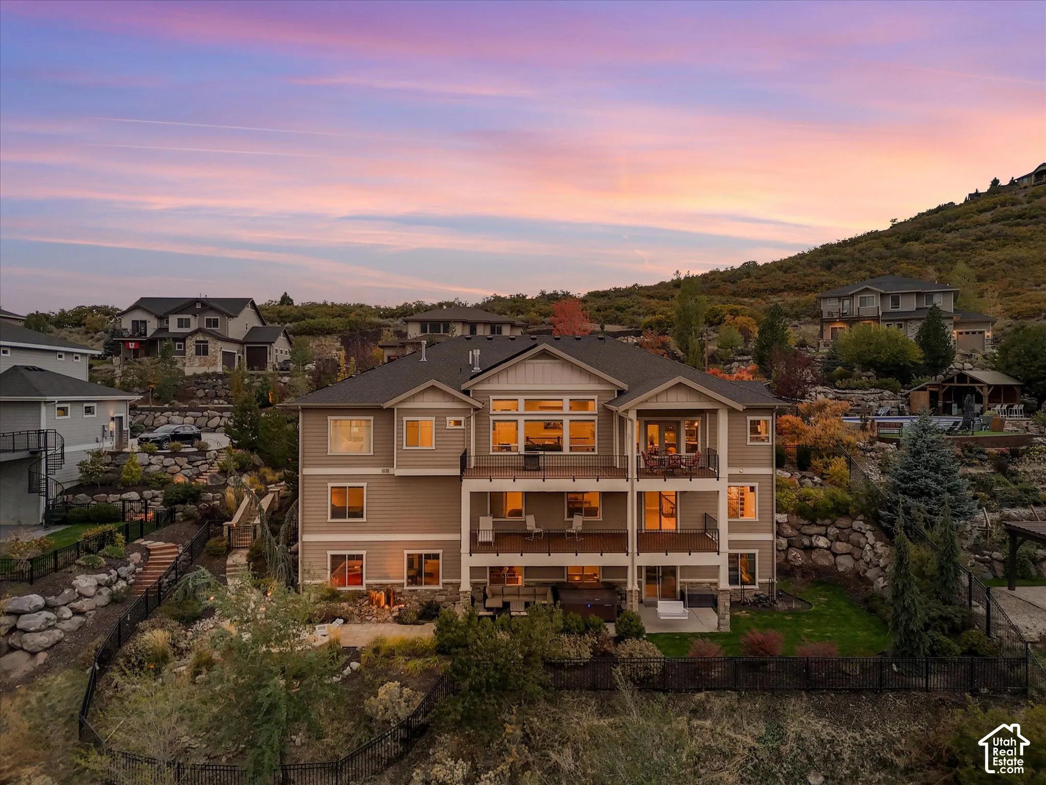 Multi-level residence featuring stacked rear decks, a covered ground-level patio, stone masonry accents, and tiered hillside landscaping