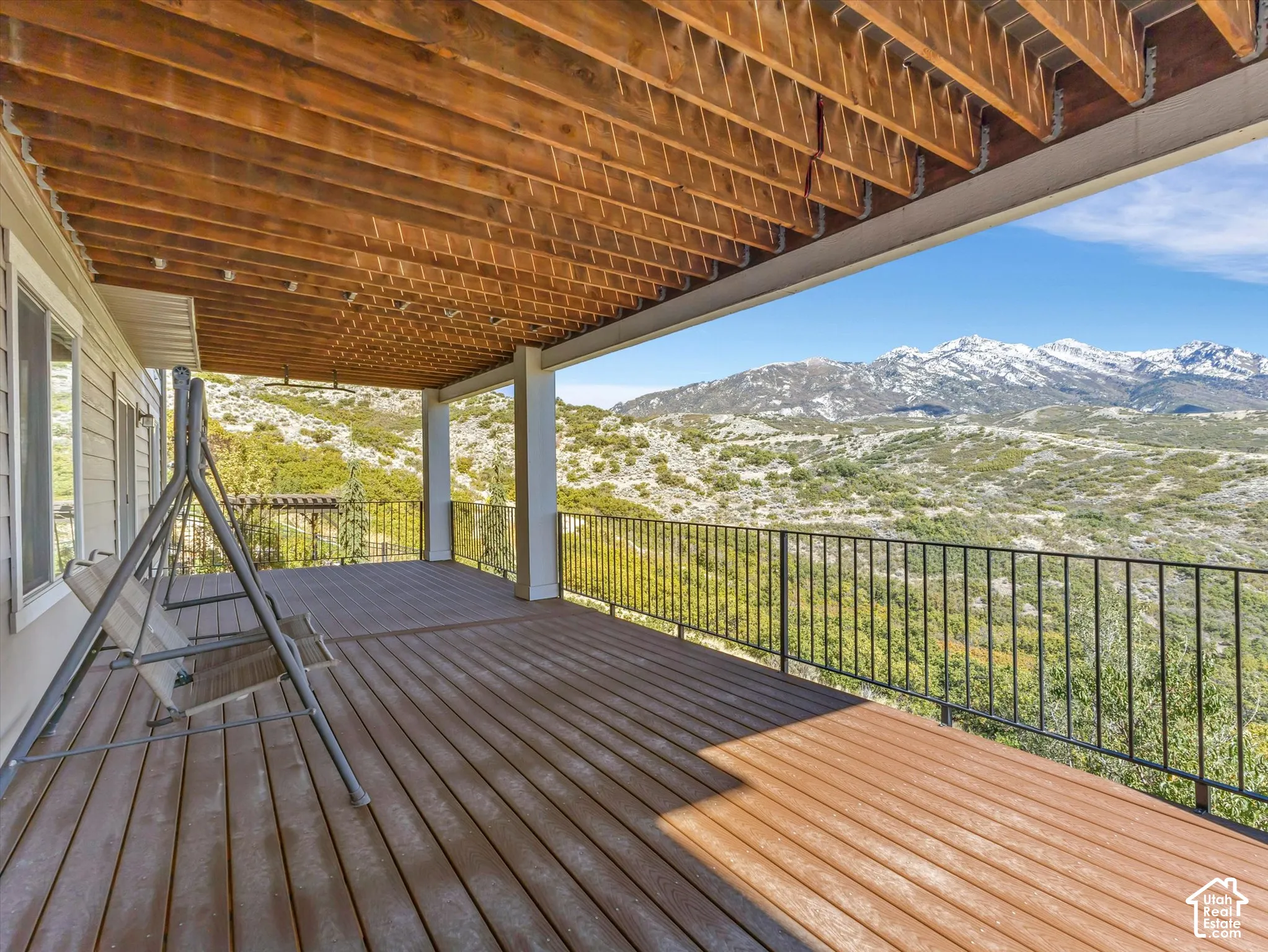 Covered deck featuring composite wood-finish decking, exposed wood beam ceiling, metal railings, and mountain backdrop