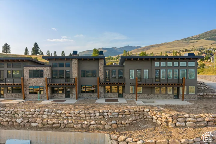 Contemporary multi-unit exterior featuring stacked stone masonry, horizontal siding, shed-style rooflines, cantilevered upper-level decks with cable railings, and a terraced stone retaining wall