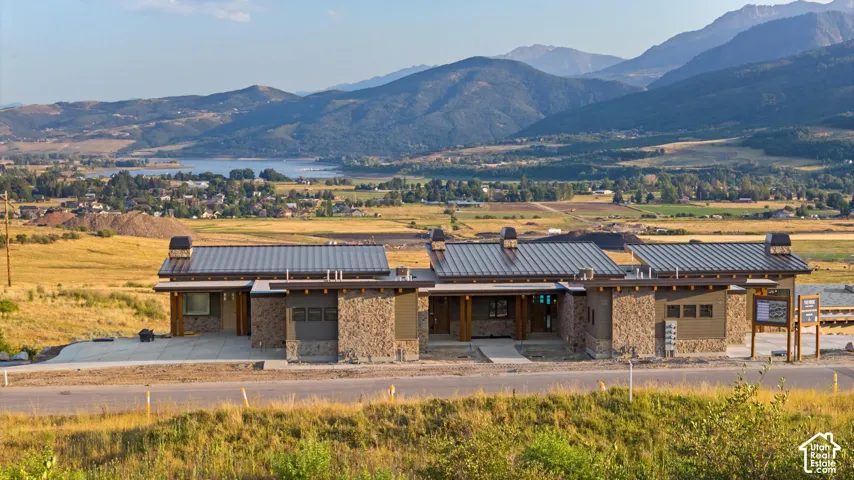 Single-level architectural design featuring stacked stone exterior veneer, metal roofing, prominent stone chimneys, and expansive mountain and valley scenery