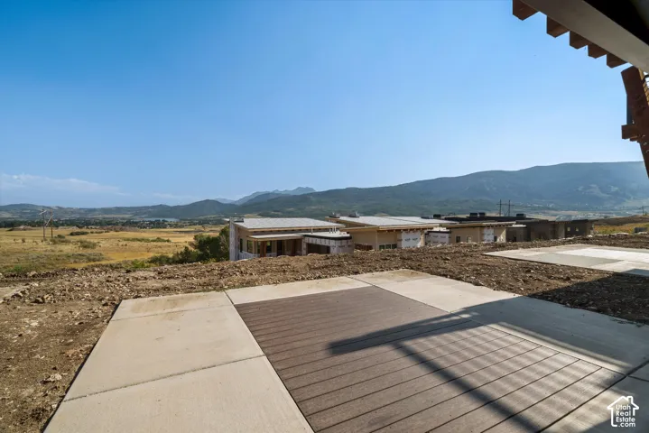 Outdoor patio featuring concrete bordering and a wood-finish inlay, complemented by wood-beam ceiling rafters and a mountain backdrop
