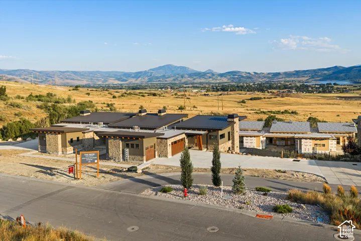 Modern architectural exterior featuring stone masonry cladding, metal shed roofing, multiple stone chimneys, and a concrete driveway, set against a mountainous horizon