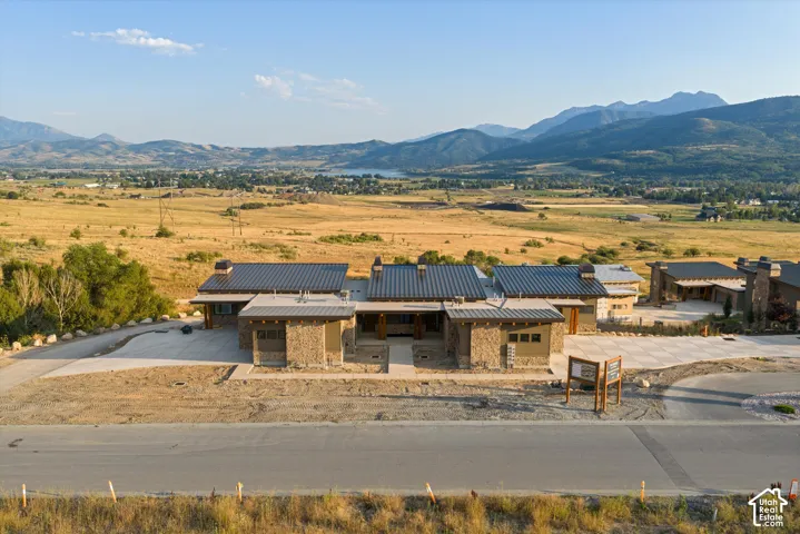 Custom architectural design featuring stone exterior cladding, multi-section metal roofing, expansive concrete driveways, and mountain backdrop