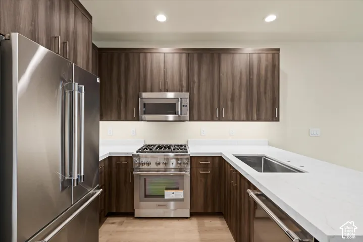 Kitchen featuring dark wood-finish cabinetry, stainless steel appliances, white solid-surface countertops, an undermount sink, and recessed ceiling lighting