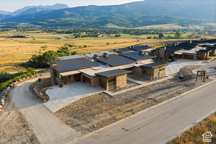 Contemporary residence featuring a multi-level metal roof, stone masonry exterior, attached multi-car garages, concrete driveways, and mountain backdrop