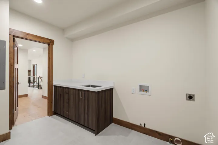 Utility room featuring dark-finish lower cabinetry, solid-surface countertop with an integrated basin, tile flooring, and natural wood door casing