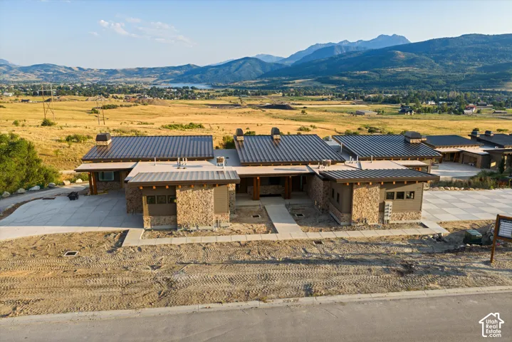 Contemporary exterior featuring stacked stone masonry, a standing-seam metal roof, exposed timber beam accents, and a concrete driveway, set against a backdrop of mountain peaks
