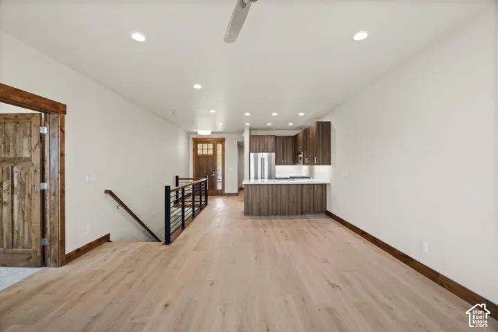 Open concept interior featuring wood-finish flooring, recessed lighting, cabinetry with stone countertops, and staircase with metal railings