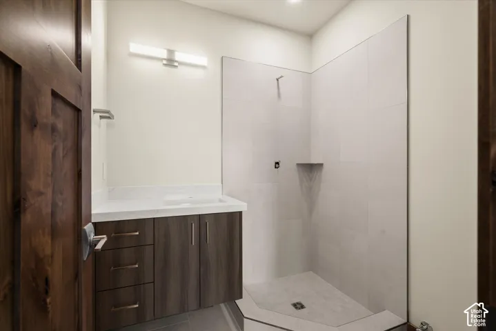 Bathroom featuring a floating vanity with dark wood-finish cabinetry, white countertop with integrated sink, linear wall-mounted lighting, and a walk-in shower with large-format tile surround