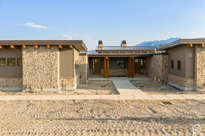 Contemporary exterior featuring natural stone veneer, horizontal wood siding, exposed timber rafter tails, a standing-seam metal roof, and mountain scenery