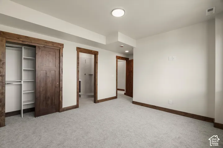 Neutral-toned carpet, natural wood door casings and trim, sliding wood-finish closet door with integrated shelving, and recessed lighting