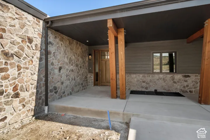 Covered entryway featuring stacked stone exterior cladding, exposed timber support columns, horizontal wood-paneled siding, and a wooden front door with glass pane detailing