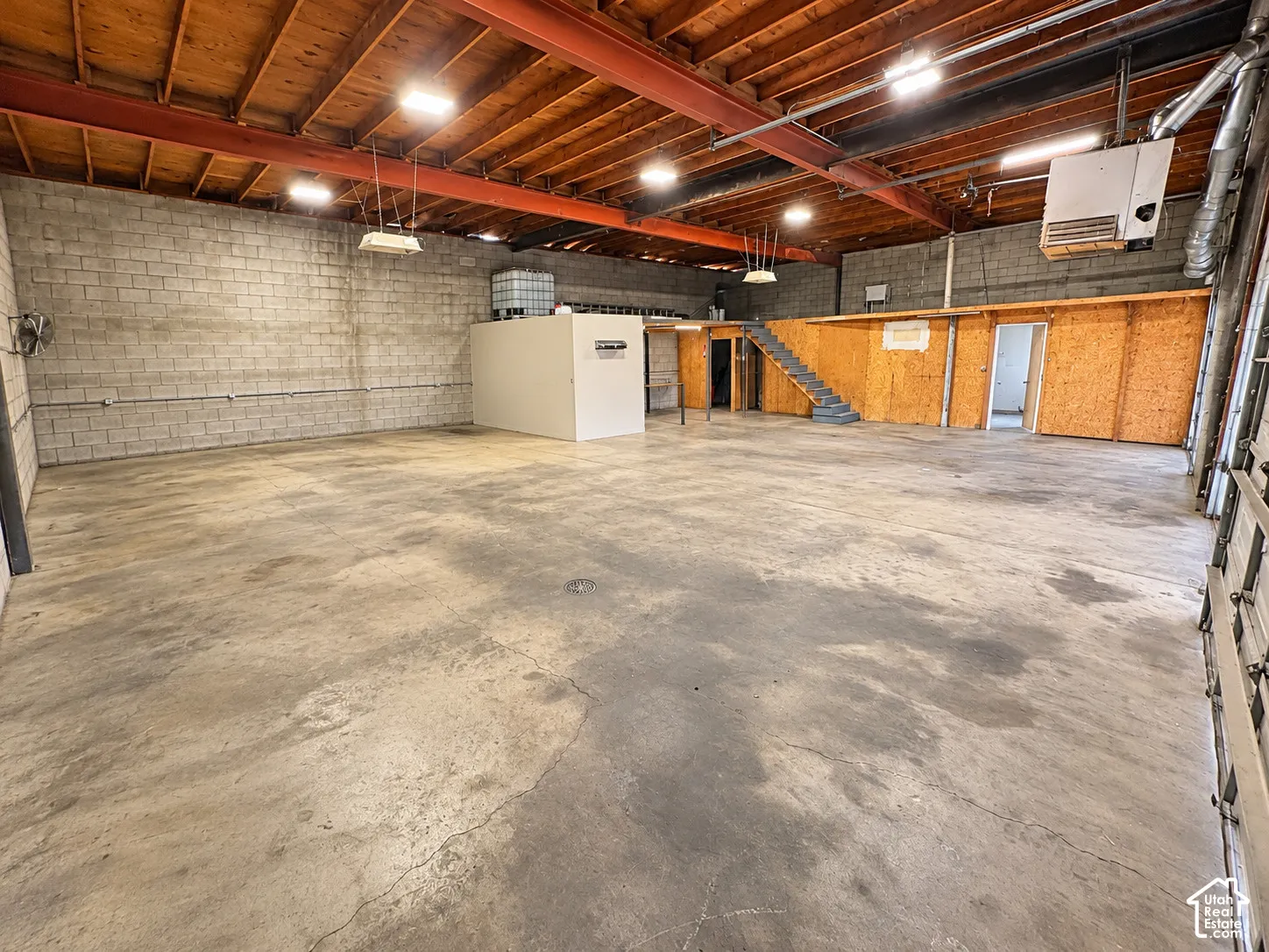 Open-span industrial interior featuring exposed wood-beam ceiling construction, polished concrete flooring, exposed masonry block walls, and integrated steel staircase