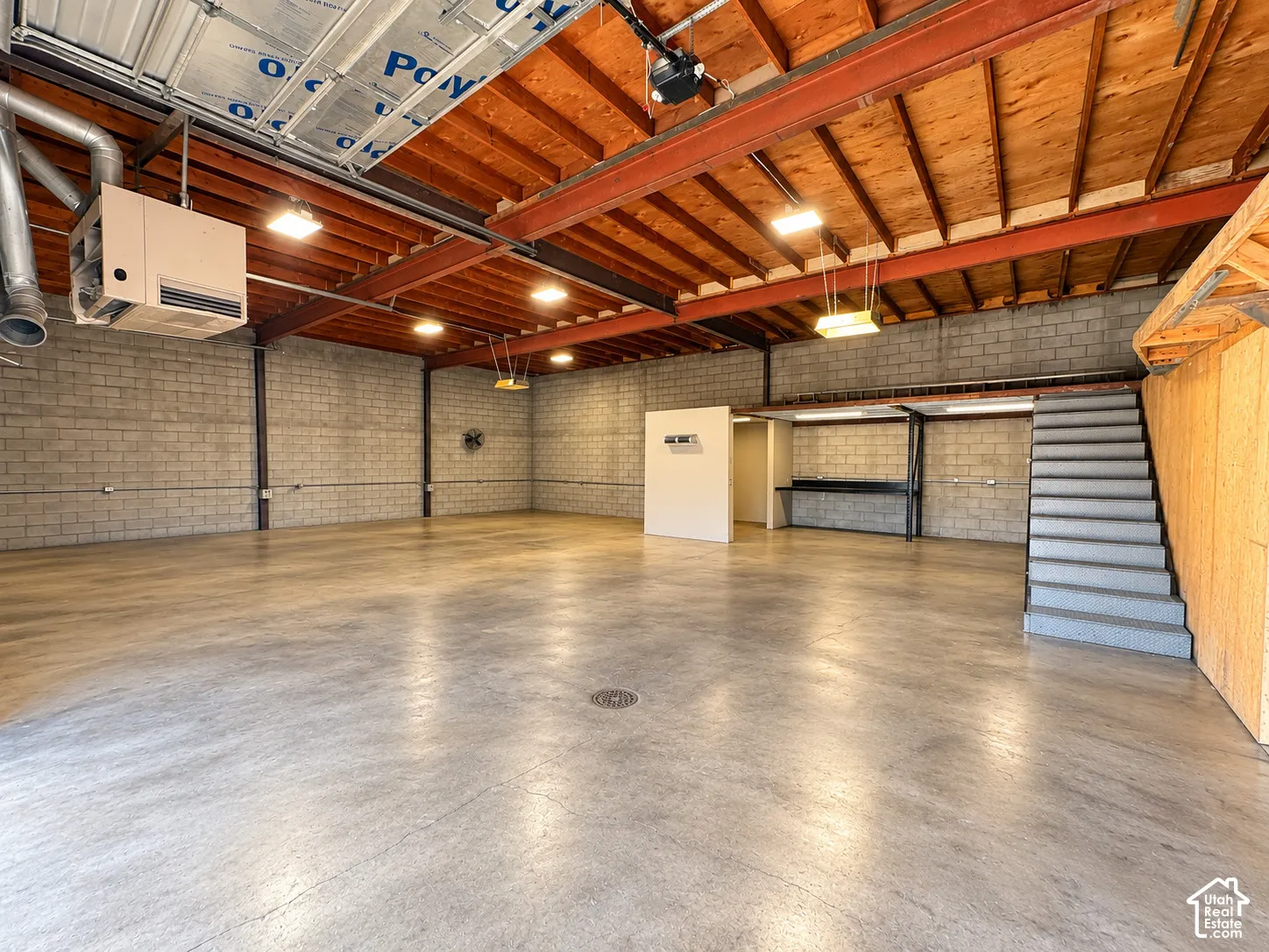 Open-concept workshop featuring exposed wood beam ceilings, concrete block walls, polished concrete flooring, and a built-in staircase