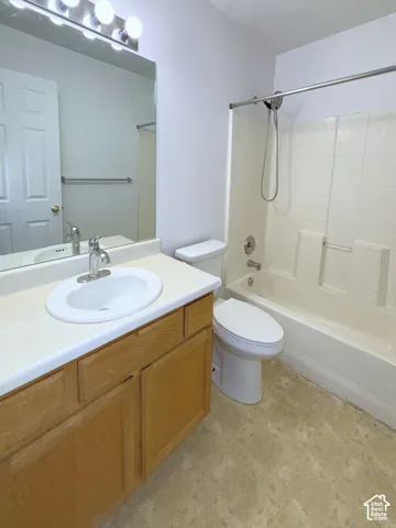 Bathroom featuring a wood-finish vanity with a molded countertop and integrated sink, full-width mirror with four-light fixture, and a tub-shower combination with a handheld showerhead