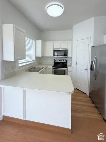 Kitchen featuring white cabinetry, solid surface countertops, wood-finish flooring, and stainless steel appliances
