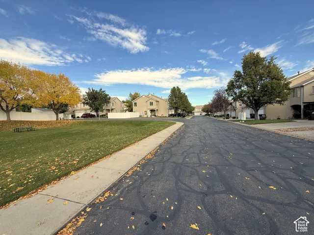Asphalt street lined with concrete sidewalks, sprawling grass common area, and mature deciduous trees
