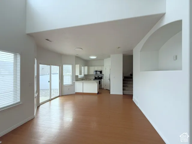 Interior featuring high vaulted ceilings, wood-finish flooring, sliding glass door access to the exterior, an arched wall niche, and kitchen cabinetry with a peninsula