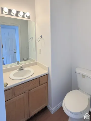 Bathroom featuring a wood-finish vanity with a composite countertop, integrated sink, four-light vanity fixture, and wood-finish flooring