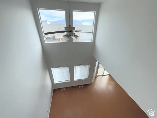 Double-height ceiling featuring floor-to-ceiling window configuration, wood-finish flooring, and a central ceiling fan with integrated lighting