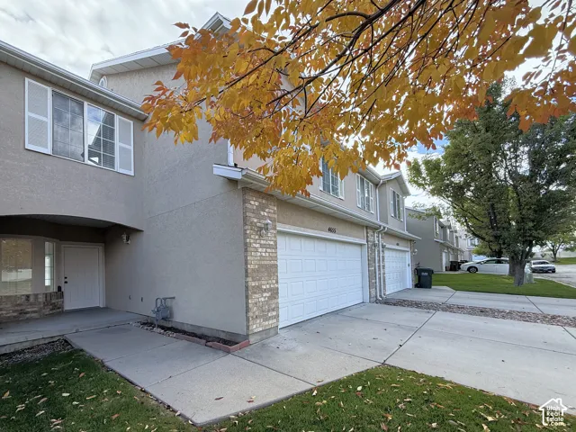 Multi-level exterior featuring stucco siding, brick veneer accents, multi-pane windows with shutters, and an attached two-car garage with concrete driveway
