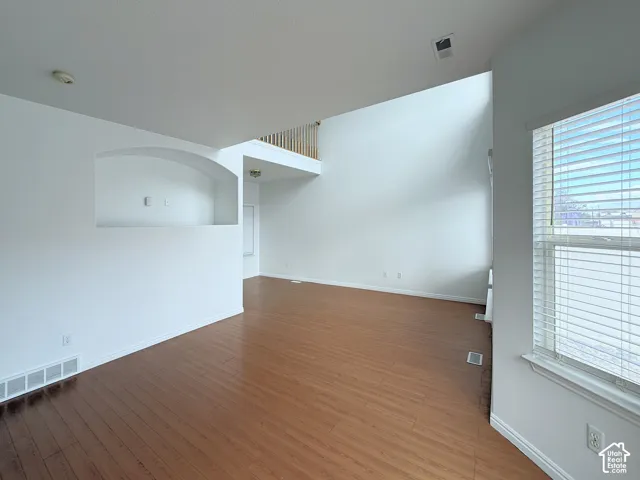 Interior featuring double-height vaulted ceilings, wood-finish flooring, a recessed wall niche, and an elevated mezzanine railing