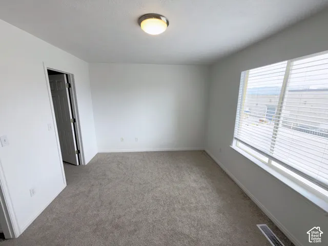 Master bedroom.Neutral-toned carpeting, large window with integrated blinds, flush-mount ceiling lighting, and a paneled interior door