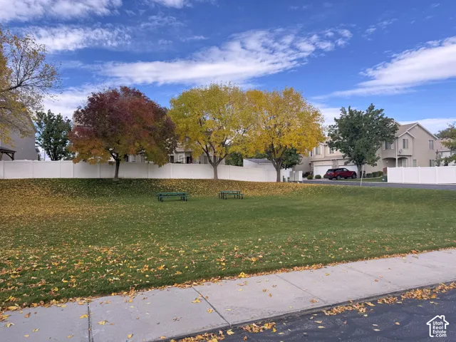 Expansive grass common area featuring mature deciduous trees and a white vinyl privacy fence