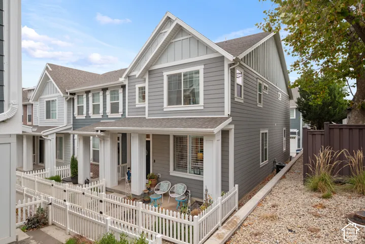 Multi-story residence featuring grey lap siding, vertical board-and-batten accents, white architectural pillars, covered porch entry, and white picket fencing