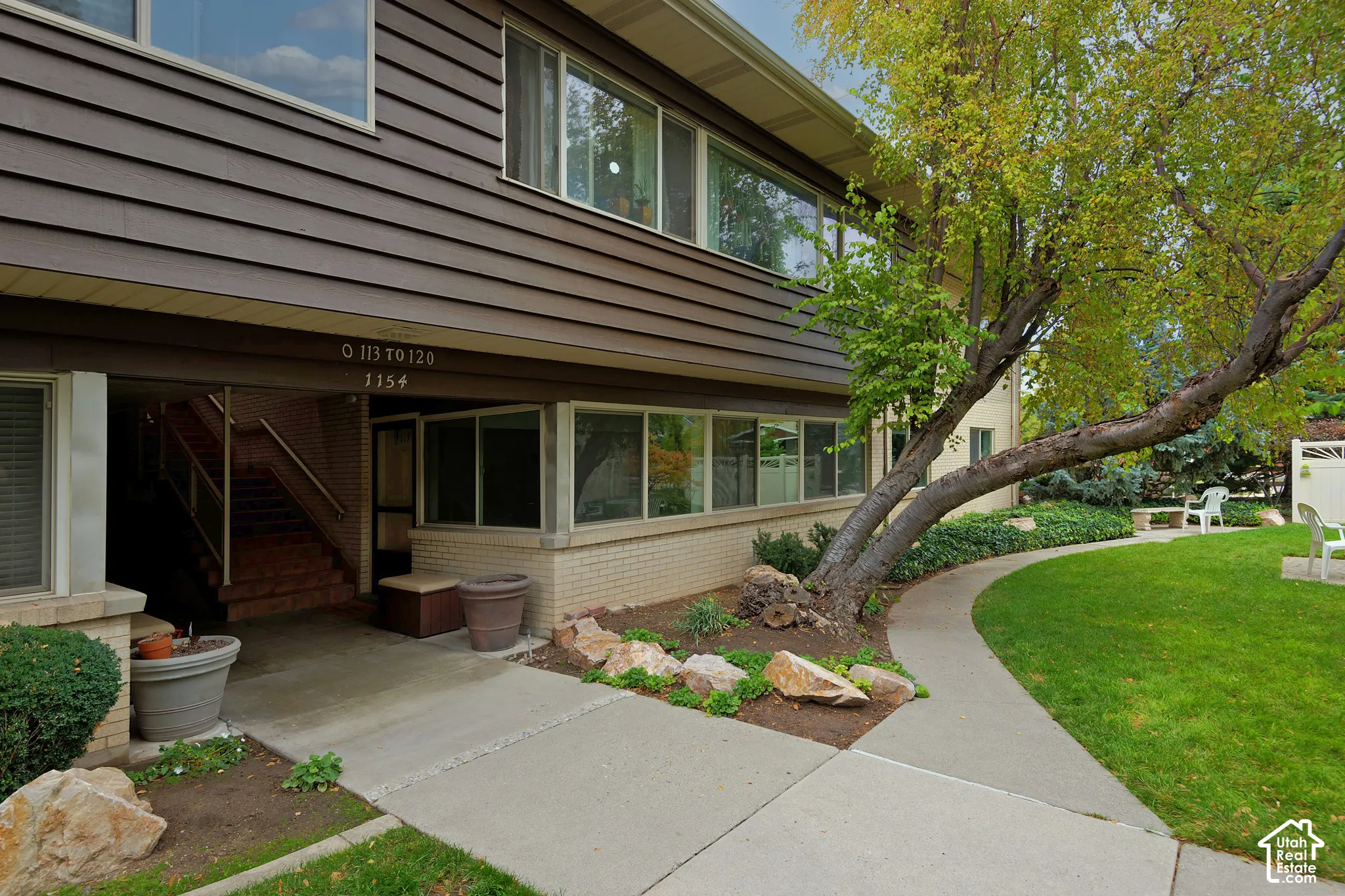 Multi-level exterior featuring dark horizontal siding, light brick masonry, extensive window glazing, and concrete pathways surrounded by landscaped grounds