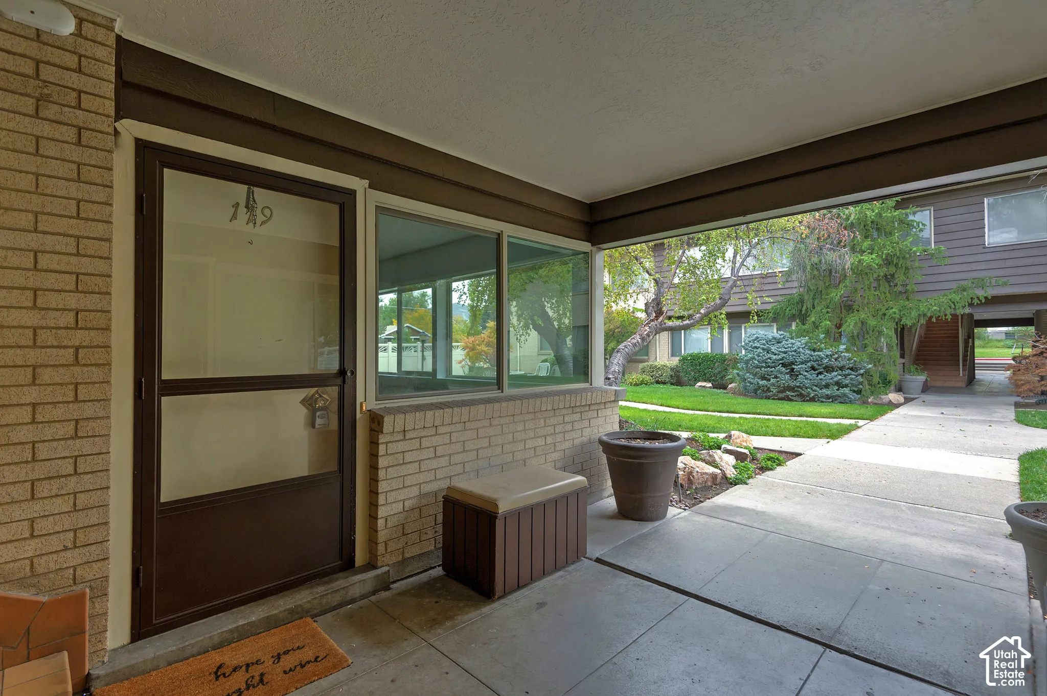Covered entryway featuring brick masonry, a storm door with glass paneling, and large-format concrete flooring