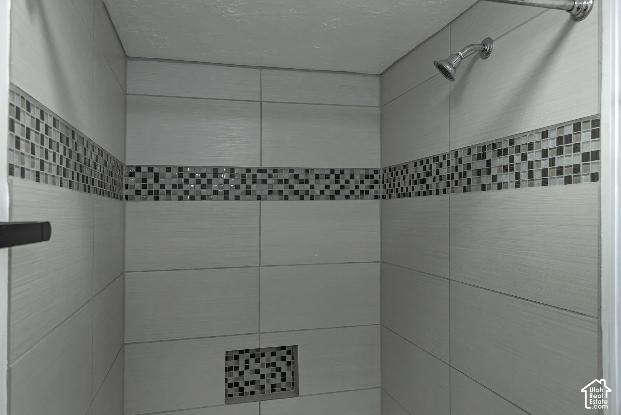 Shower featuring large-format ceramic wall tile, decorative mosaic tile inlay, integrated wall niche, and polished chrome shower head