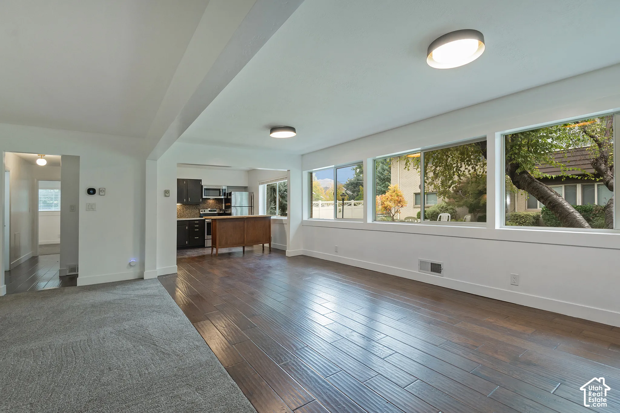 Open living area featuring wood-finish flooring, extensive sliding glass windows, recessed ceiling lighting, and dark cabinetry in the kitchen area